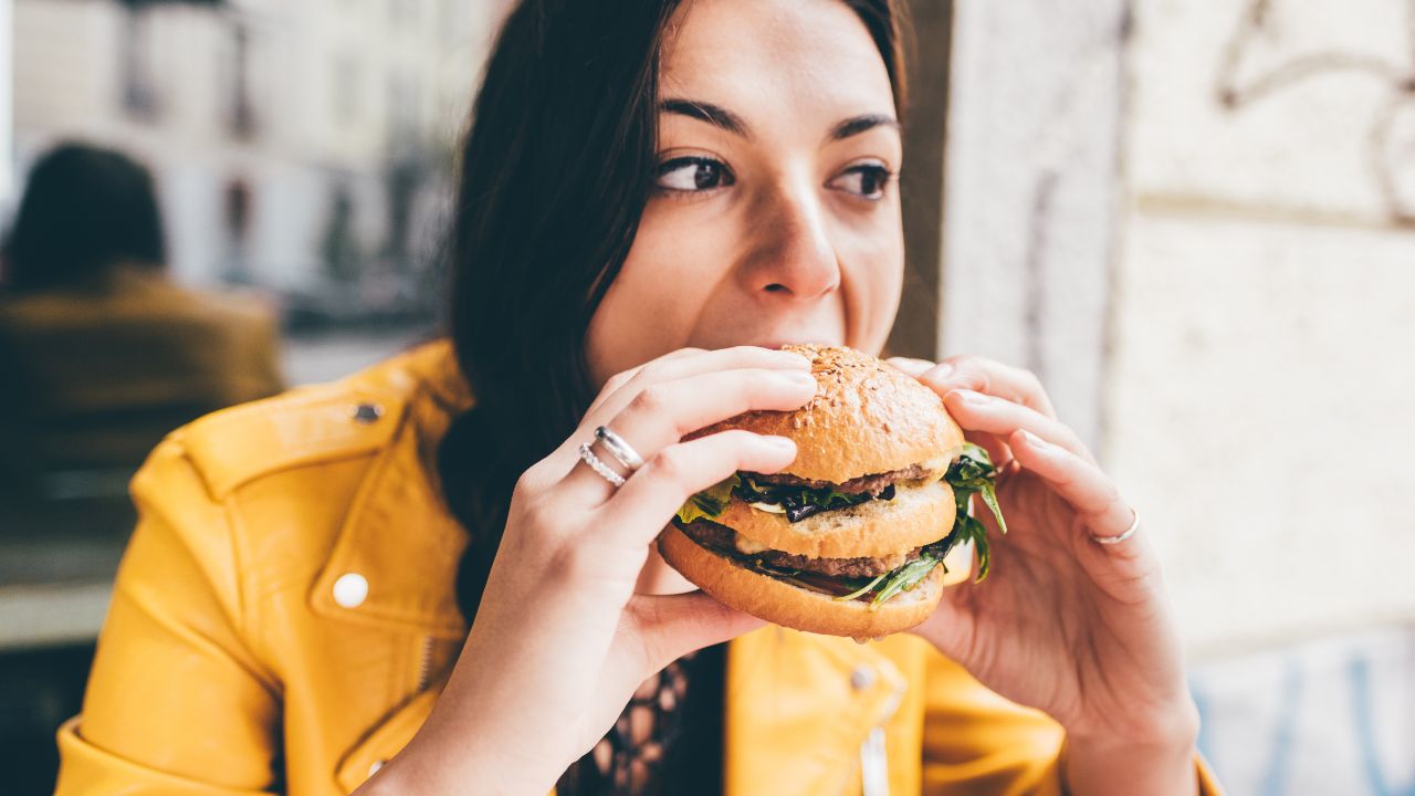 Alimentos que não se comem de estômago vazio. Mulher comendo um hambúrguer.