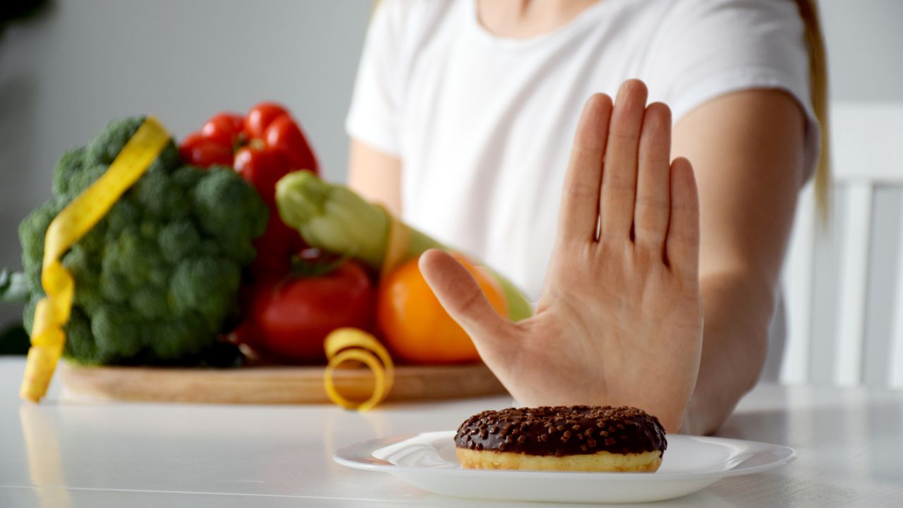 Dieta. Mulher estende a mão aberta em referência ao gesto "Pare" para um alimento calórico.